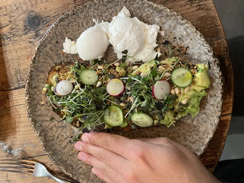 Avocado toast with poached eggs, micro-greens and cucumber on a plate